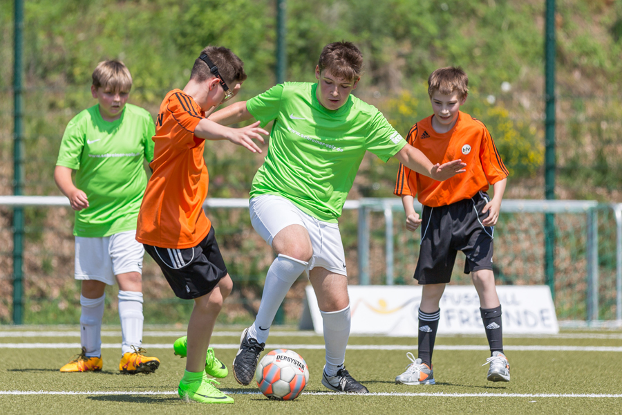 Jungen spielen Fußball auf einem grünen Rasenfeld, ein Junge dribbelt den Ball und wird von Gegenspielern angegriffen.