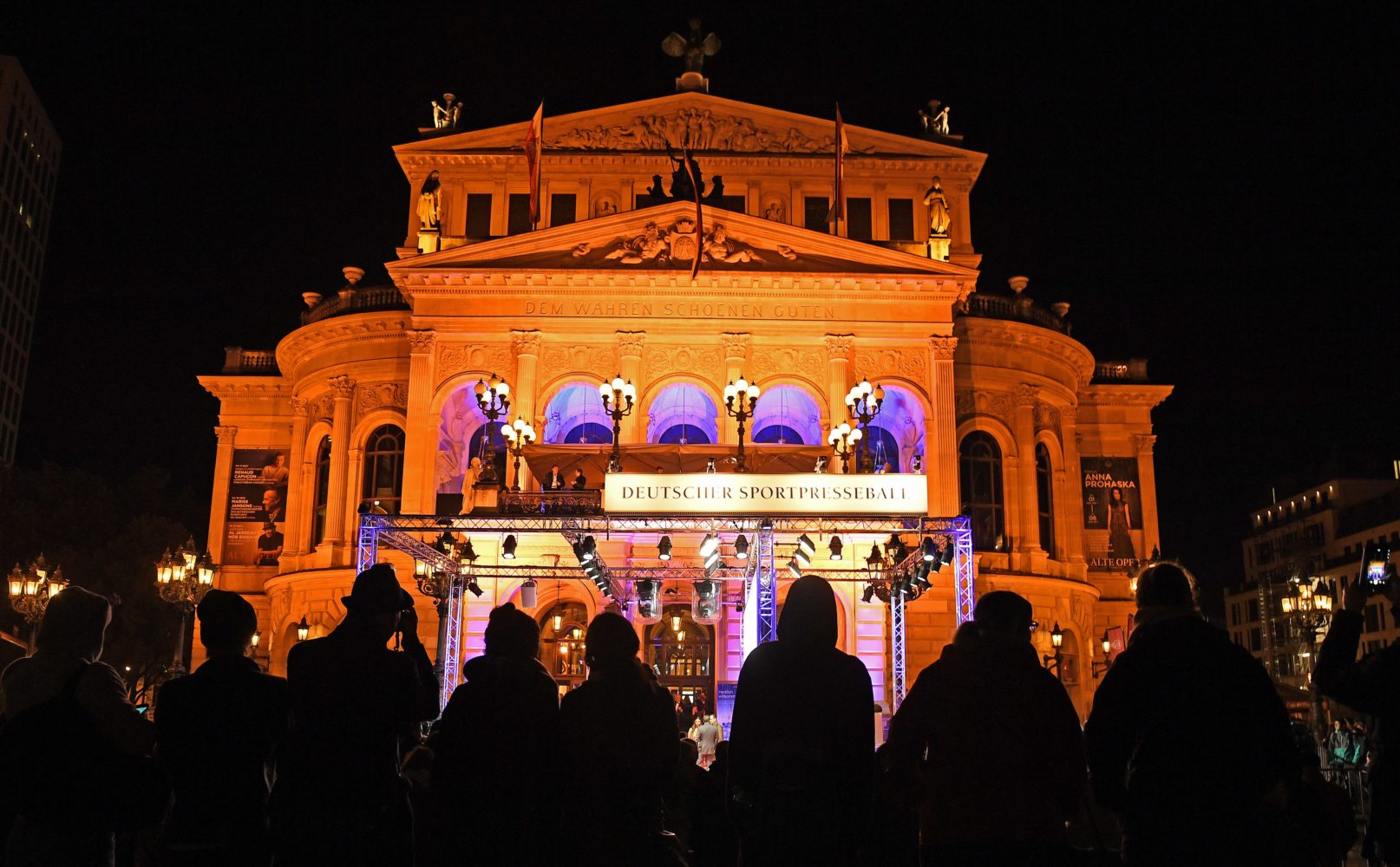 Aussenansicht der Alten Oper in Frankfurt bei Nacht, beleuchtet für den 35. Deutschen Sportpresseball. Zahlreiche Personen stehen vor dem Gebäude und fotografieren mit ihren Handys.