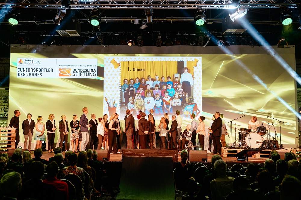 Junge Sportler und Sportlerinnen stehen auf einer Bühne und werden für ihre Leistungen geehrt. Im Hintergrund eine Leinwand mit dem Titel "Juniorsportler des Jahres" und dem Logo der Deutschen Sportstiftung und der Bundesliga Stiftung.