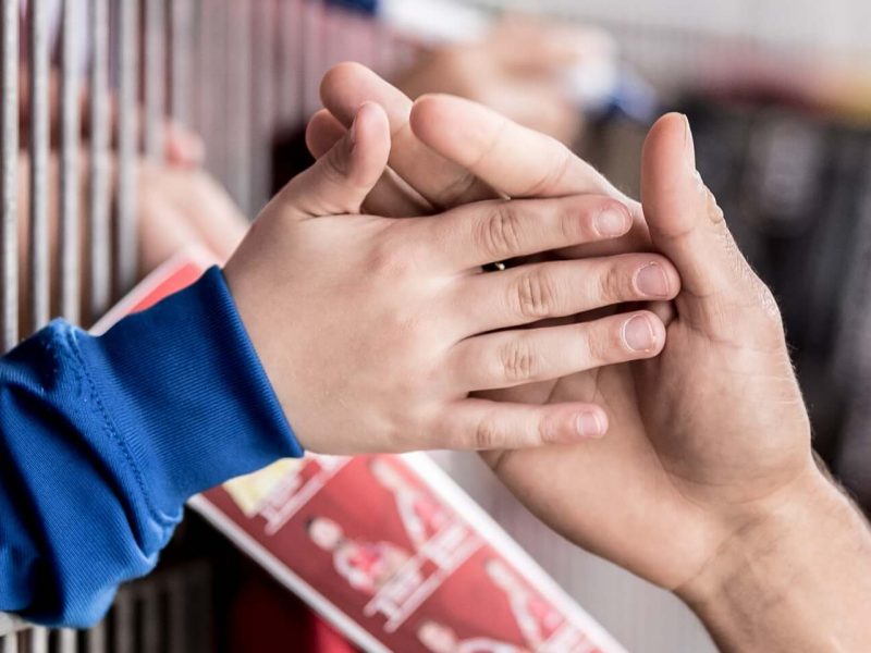 Hände, die sich berühren, vor einem unscharfen Hintergrund von Menschen und Strukturen.