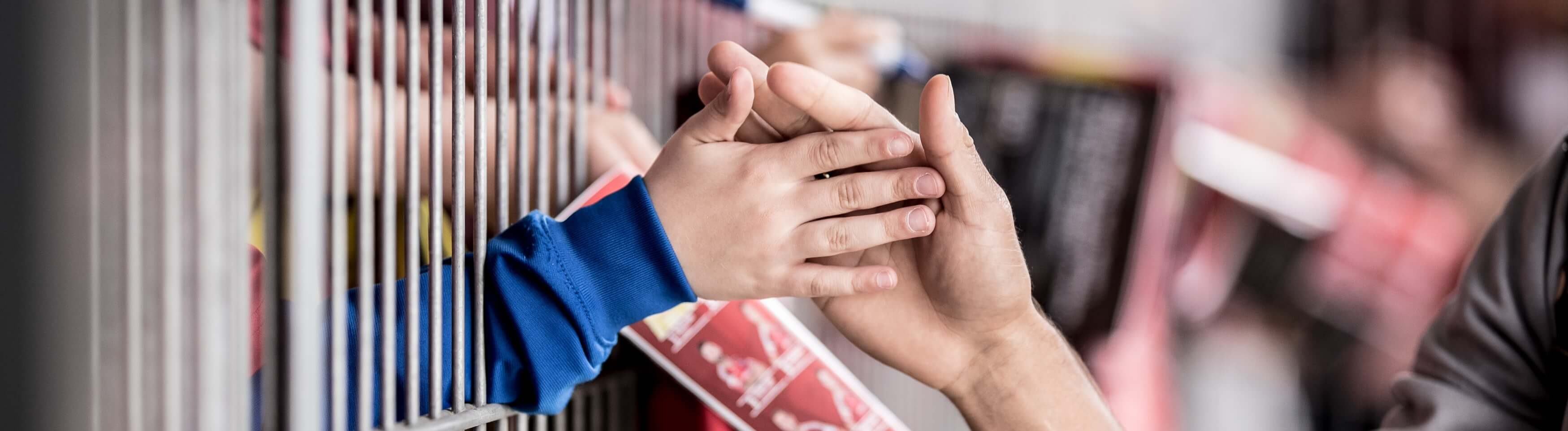 Hände, die sich berühren, vor einem unscharfen Hintergrund von Menschen und Strukturen.