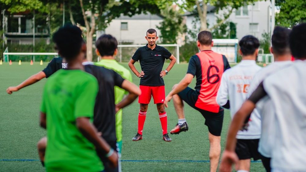 Der Trainer steht vor dem Team auf einem Fußballfeld.