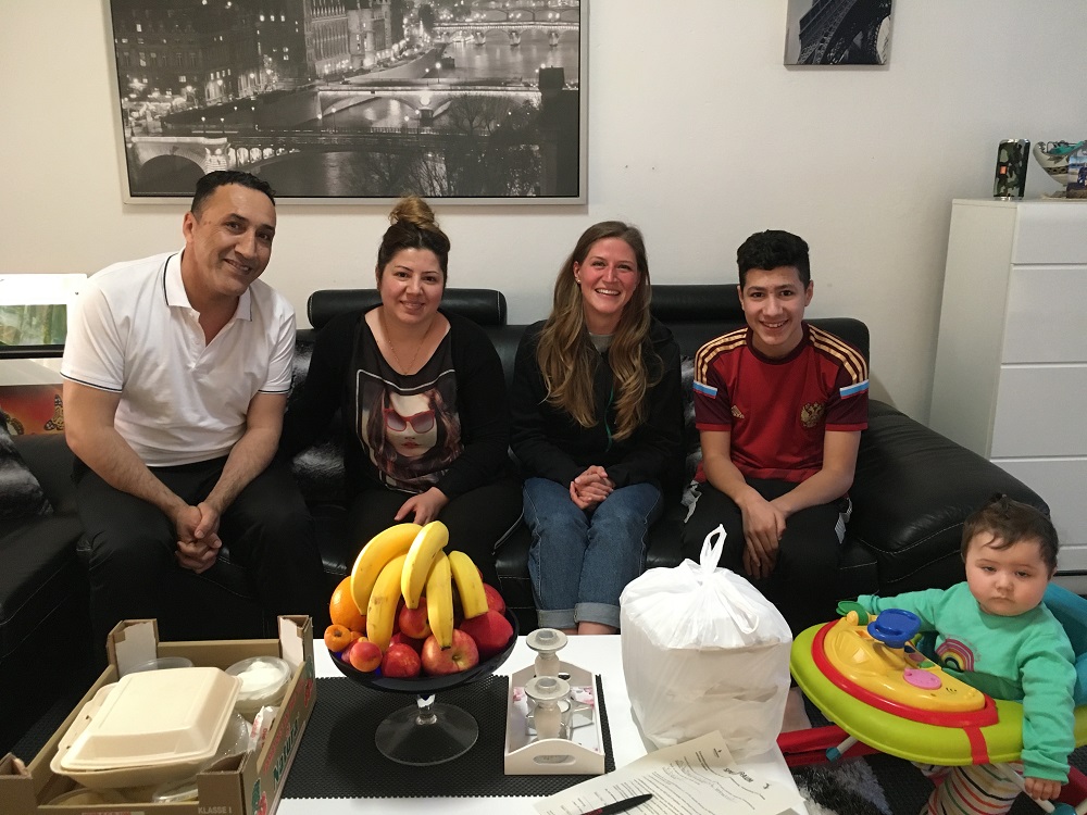 Ein Mann, zwei Frauen und ein Junge sitzen auf der Couch und lächeln, während das kleine Kind im Kinderstuhl sitzt.