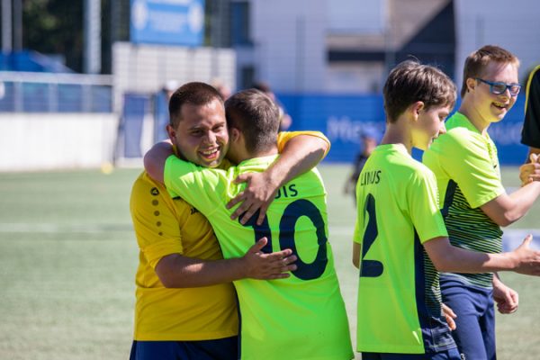 Im Vordergrund umarmen sich zwei Fußballspieler mit gelben Trikots. Im Hintergrund geben sich drei weitere Jungs die Hände.