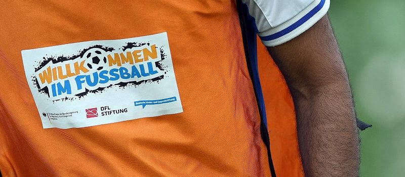 Ein Mann im orangenen Trikot mit dem Aufkleber "Willkommen im Fußball"