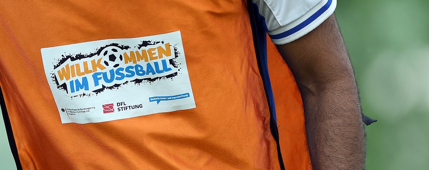 Ein Mann im orangenen Trikot mit dem Aufkleber "Willkommen im Fußball"