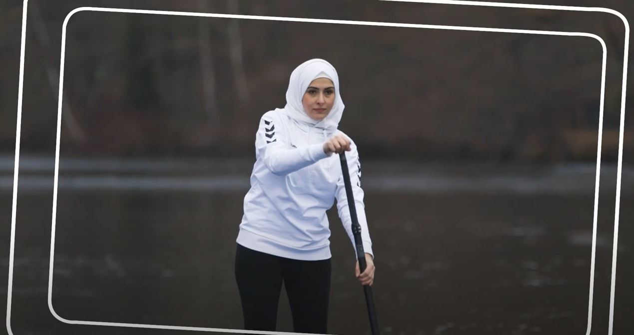 Mädel im weißen Sweatshirt und mit weißem Kopftuch paddelt auf dem See