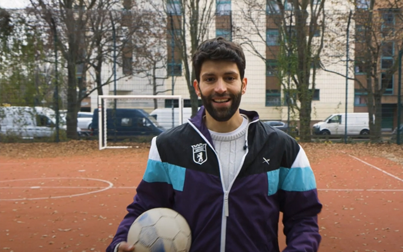 Student Saeed steht auf dem Fußballfeld und hält den Fußball in seiner rechten Hand