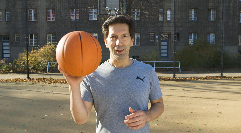 Sport- und Gymnastiklehrer steht hält den Basketball in seiner rechten Hand