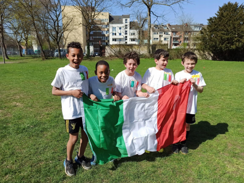 Fünf kleine Jungen halten die italienische Flagge auf einem Fußballfeld