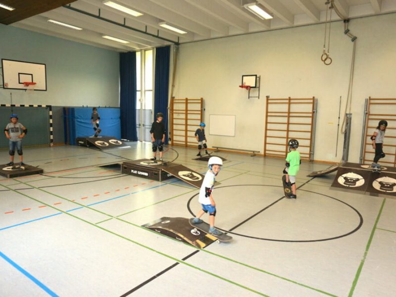 Schüler mit Schutzhelmen fahren Skateboards in der Turnhalle