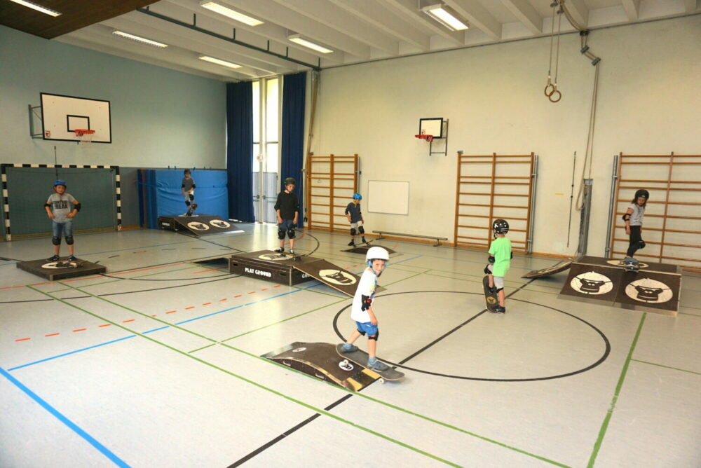 Schüler mit Schutzhelmen fahren Skateboards in der Turnhalle