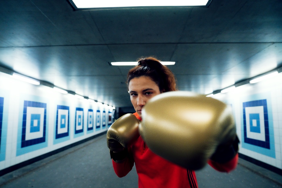 Boxerin Sarah Scheurich boxt mit ihrer linken Hand in Richtung Kamera. Sie trägt ein rotes Oberteil und goldene Box-Handschuhe.