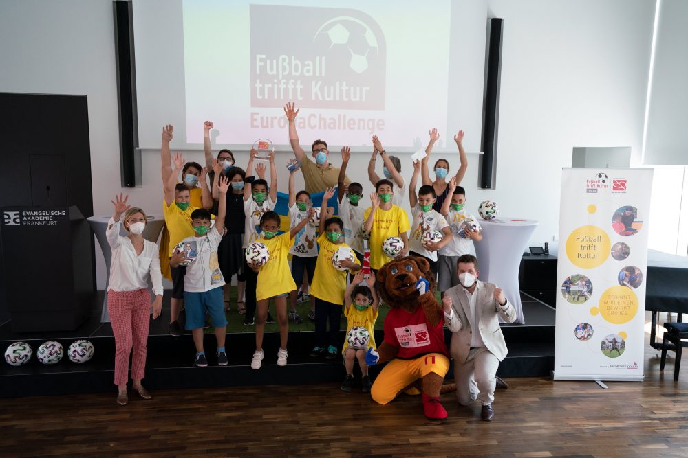 Schüler der Karmeliterschule winken mit den Jurymitgliedern und der Maskotte des Programmes ,,Fußball trifft Kultur"