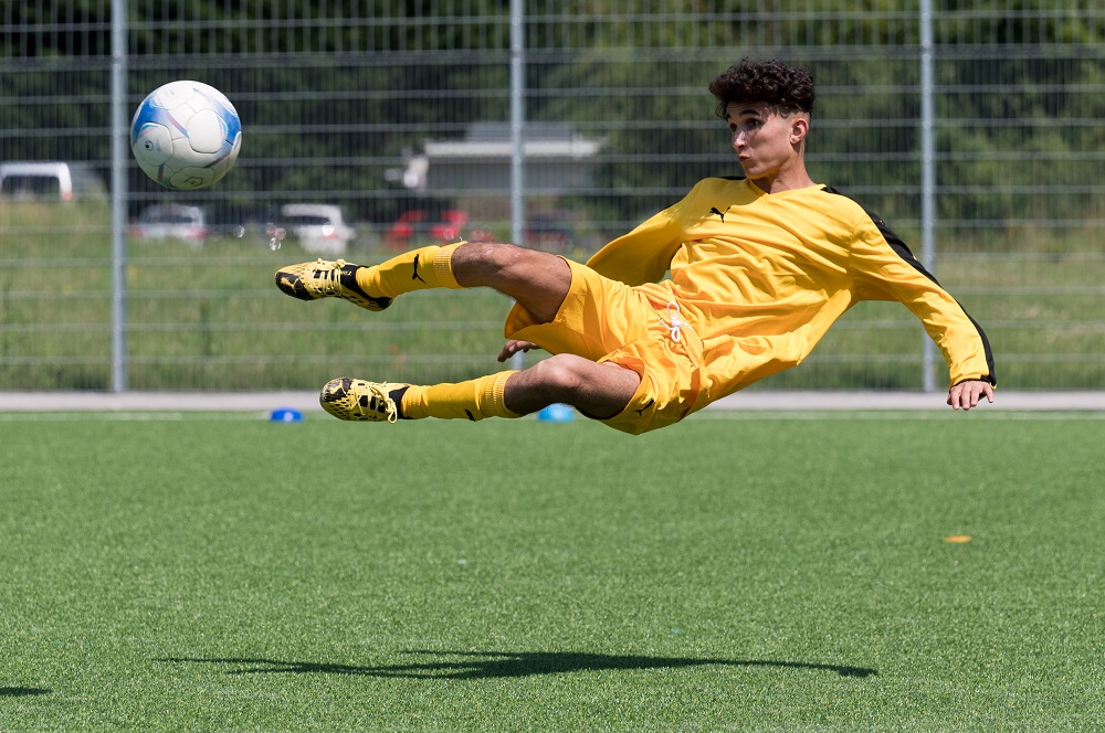 Junge im gelben Trikot kickt den Ball in der Luft.