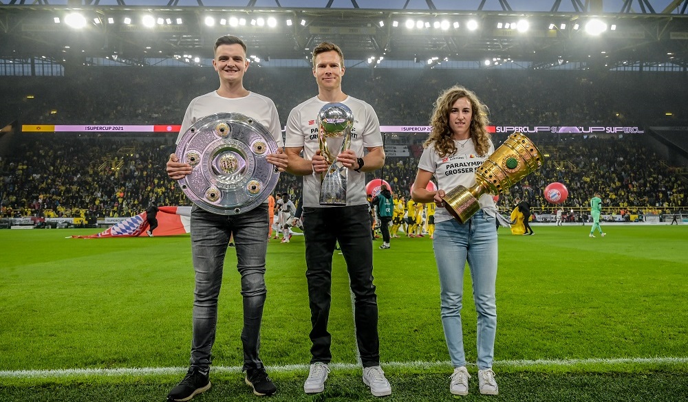 Yannik Rüddenklau (links), Markus Rehm (Mitte) und Anna-Maria Rieder (rechts) präsentieren die Trophäen des deutschen Fußballs auf dem Rasen im Signal Iduna Park.