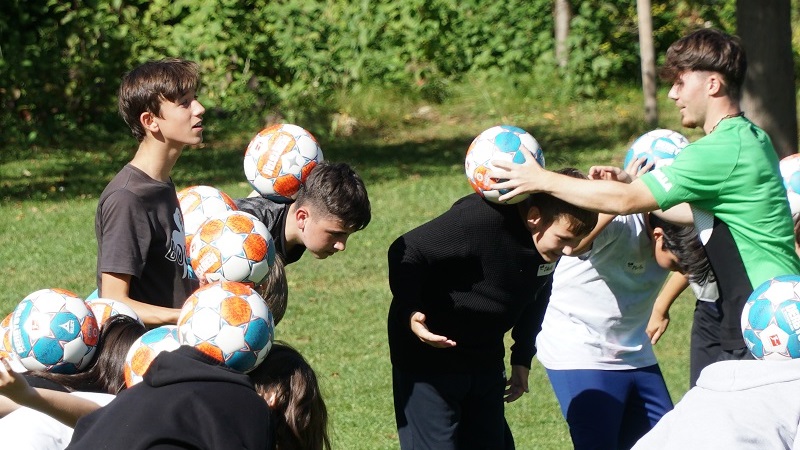 Young people can be seen trying to balance a soccer ball on their backs.