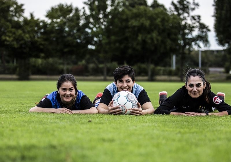 Drei Mädchen liegen auf dem Fußballfeld und lächeln