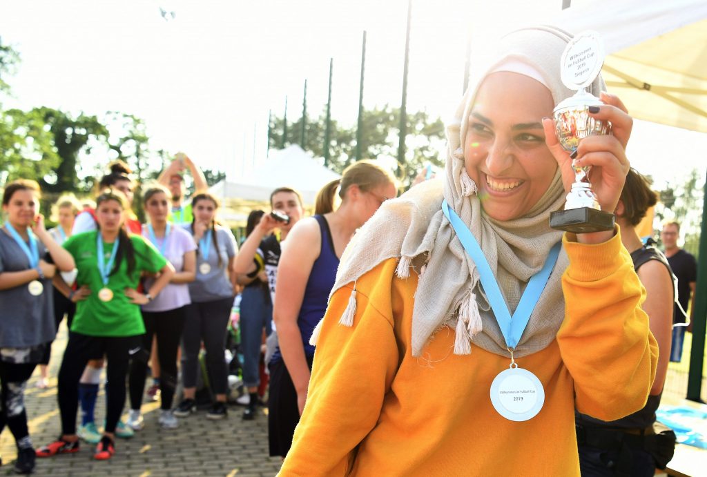 Mädchen mit Kopftuch lacht und zeigt ihr Pokal.