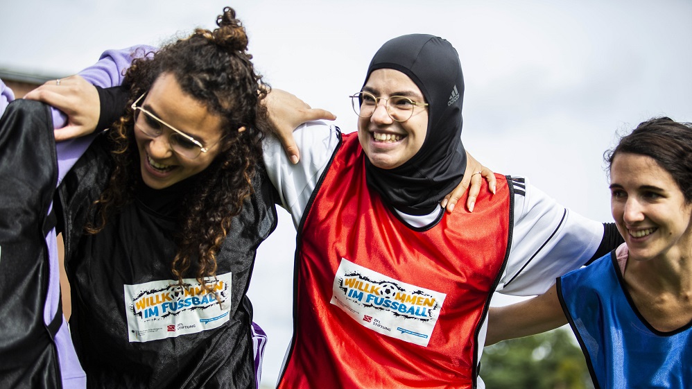 Drei junge Frauen, die die Arme über die Schultern der anderen gelegt haben.