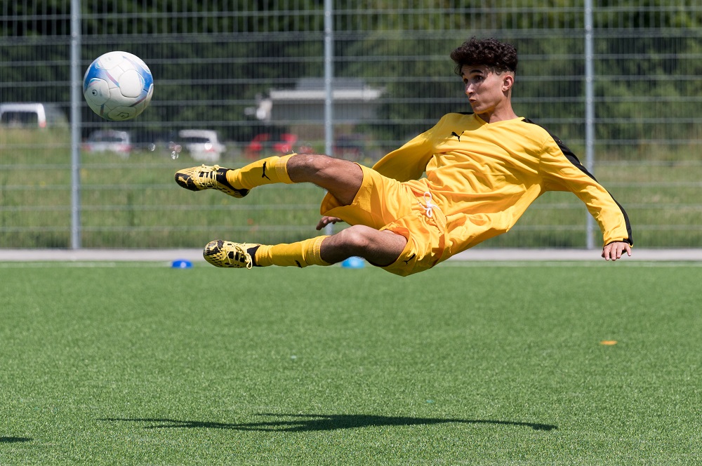 Ein Fußballspieler im gelben Trikot liegt seitlich in der Luft und schießt einen Ball.