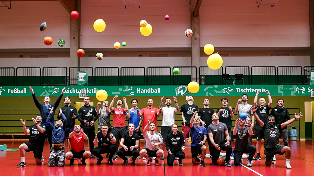 Die Teilnehmenden der Qualifizierungsveranstaltung werfen nach einer Sporteinheit bunte Luftballons in den Turnhallen-Himmel.