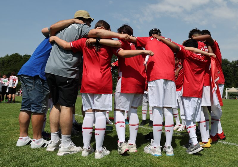 Ein Team steht im Kreis. Die Spielerinnen und Spieler haben die Arme über die Schultern gelegt.