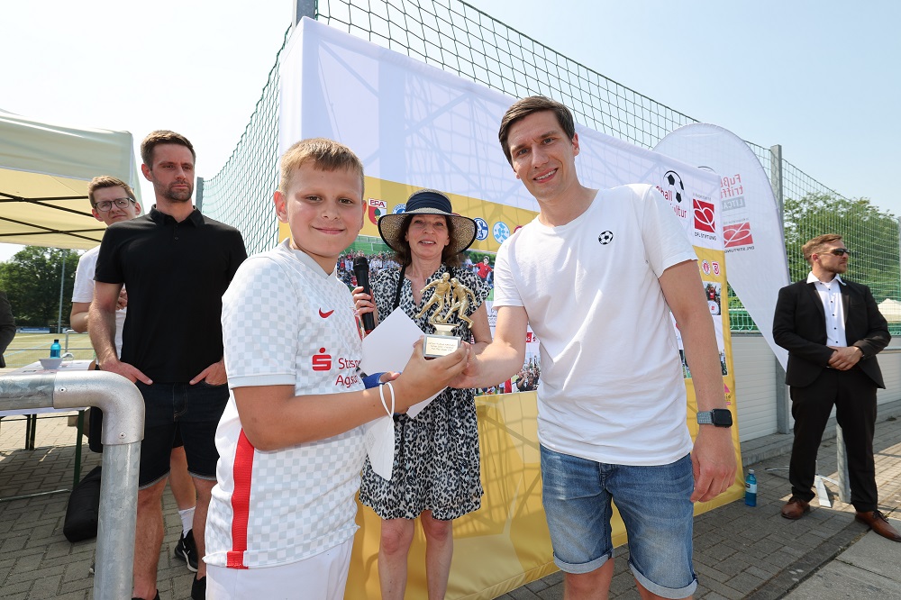 Ein Junge erhält einen Pokal von einem Mann.