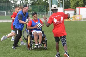 Verschiedene Spieler, davon einer im Rollstuhl, spielen mit einem Fußball.