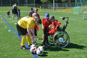 "Willkommen im Fußball"-Banner im Hintergrund einer Veranstaltung, auf dem das Engagement für junge Geflüchtete hervorgehoben wird. Im Vordergrund liegen Broschüren und Informationsmaterialien zur Integration durch Fußball.