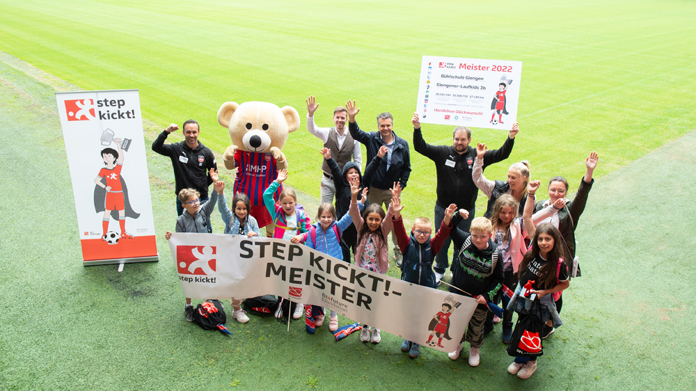 Die Sieger der step kickt!-Challenge aus Heidenheim stehen mit Bannern auf dem Stadionrasen und freuen sich.