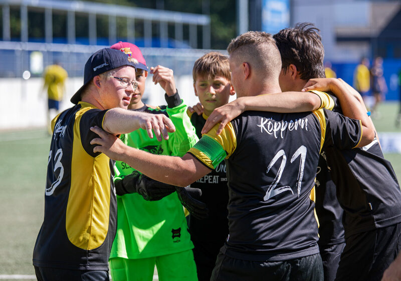 Fünf junge Fußballspieler stehen auf dem Fußballplatz im Kreis und haben die Arme über die Schultern gelegt.