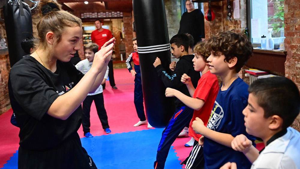 Lena Büchner (links) steht vier Jungs (rechts) in einer Boxhalle gegenüber und wehrt deren Schläge ab.