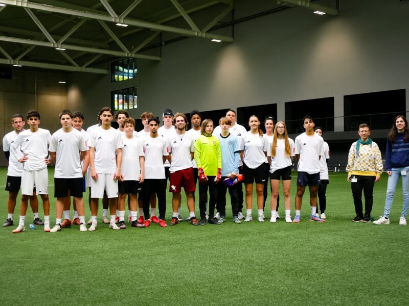 Eine Gruppe junger Menschen steht in Trikots aufgereiht auf einem Fußballplatz